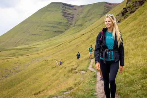 Woman walking along a dirt trail, with a grassy hill behind her
