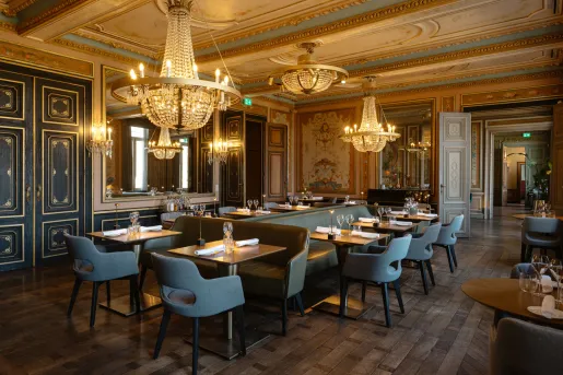 Dimly lit restaurant with wooden tables and gray, cushioned chairs