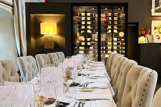 Restaurant dining room with a long dining table and cushioned, beige chairs