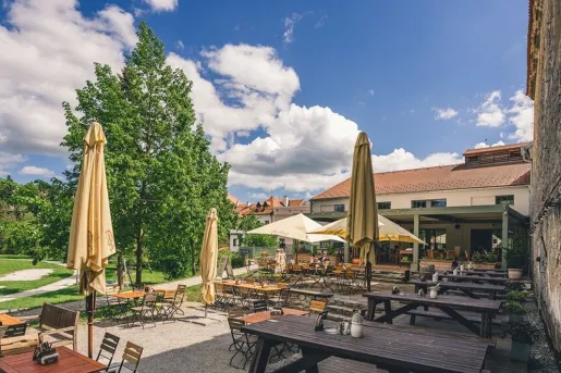The outdoor terrace restaurant, featuring large beige umbrellas and wooden picnic tables at Boutique Hotel Latrán in Český Krumlov, Czech Republic.