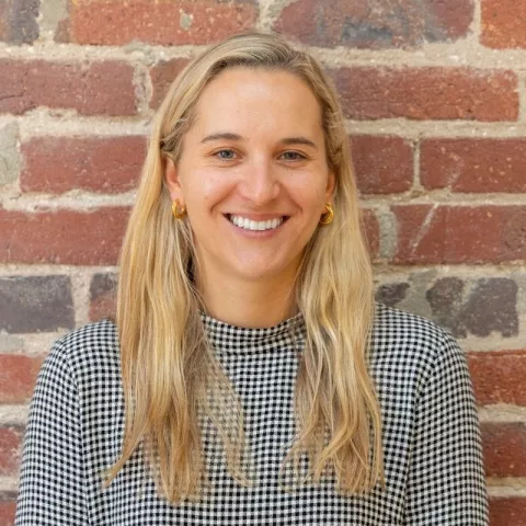Woman with blonde hair, smiling in front of a brick wall