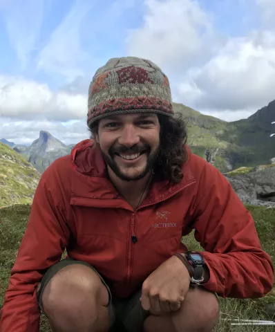 Man in a red jacket, smiling while standing on top of a hill
