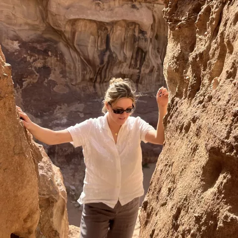 Woman wearing a white shirt and sunglasses, walking up on a canyon
