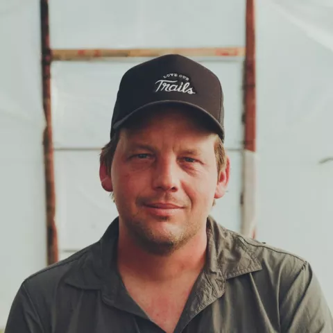 Man wearing a hat, sitting inside of a greenhouse with plants