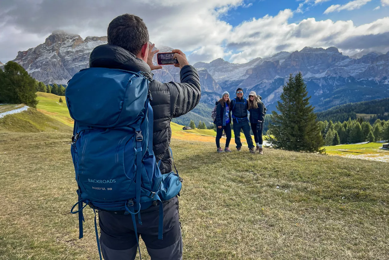 One guest taking photo of other three, mountains behind them.