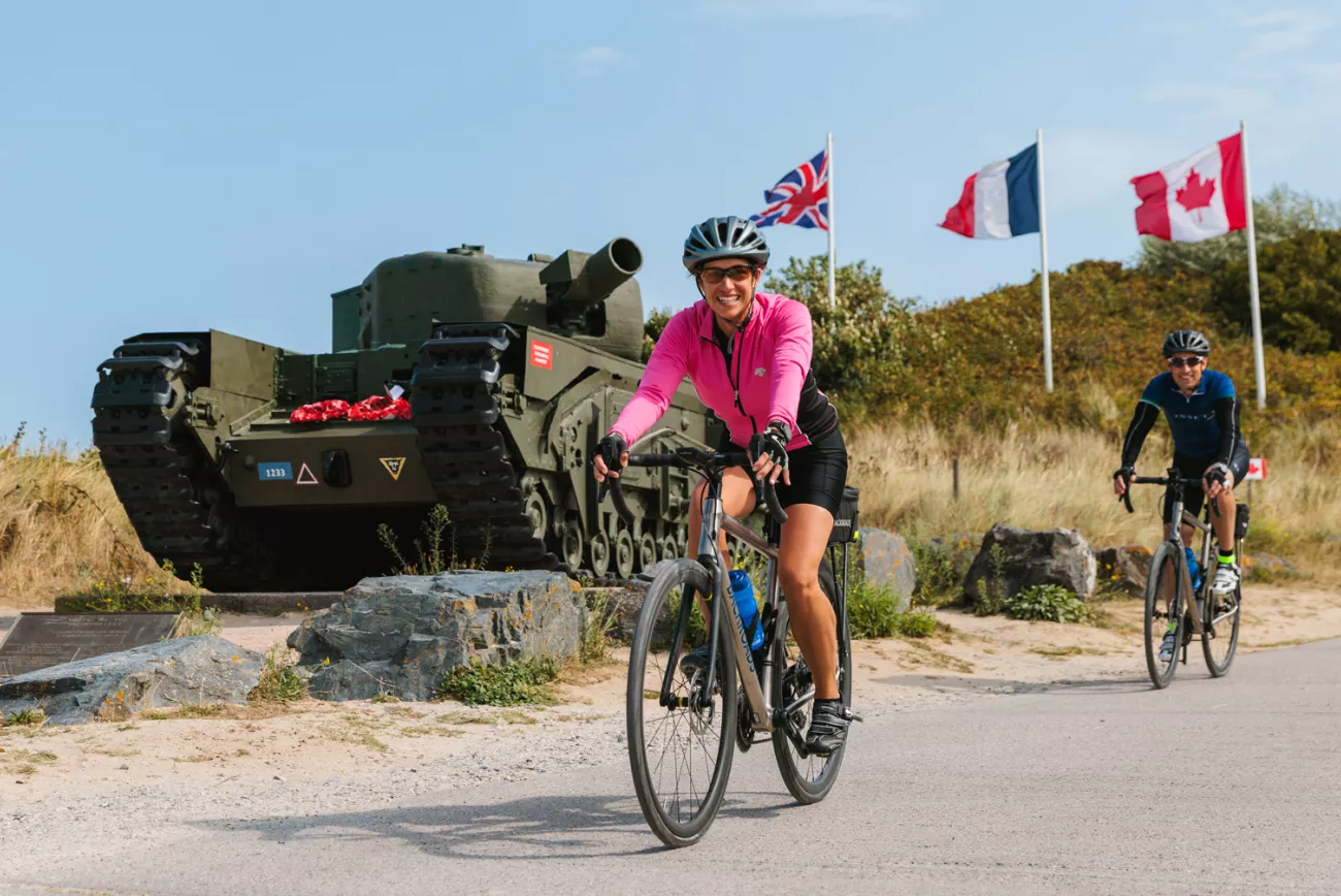 Woman in pink, biking in front of a green tank with flags waiving in the background