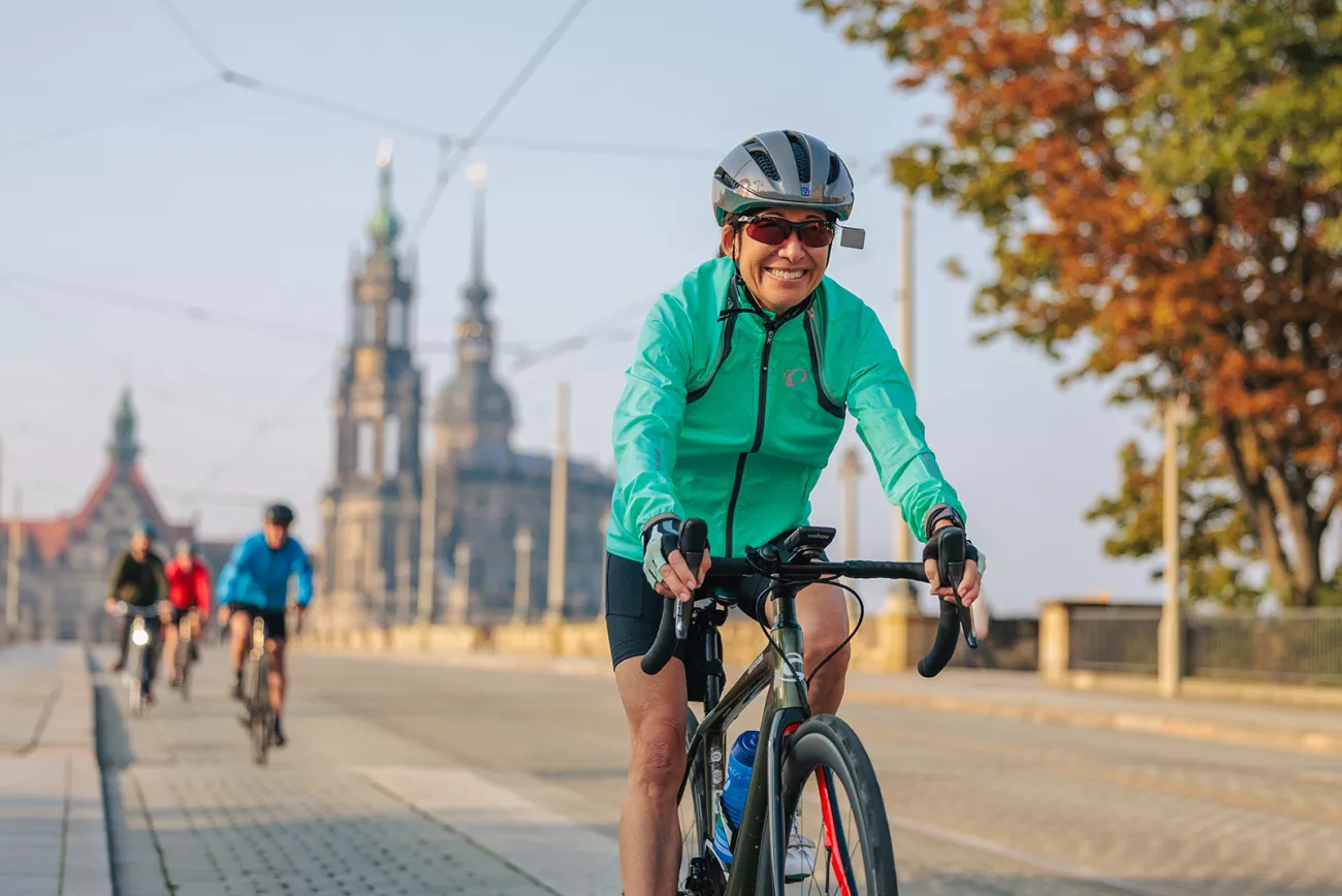 Woman wearing a green jacket, smiling while riding a bike and a cathedral in the background