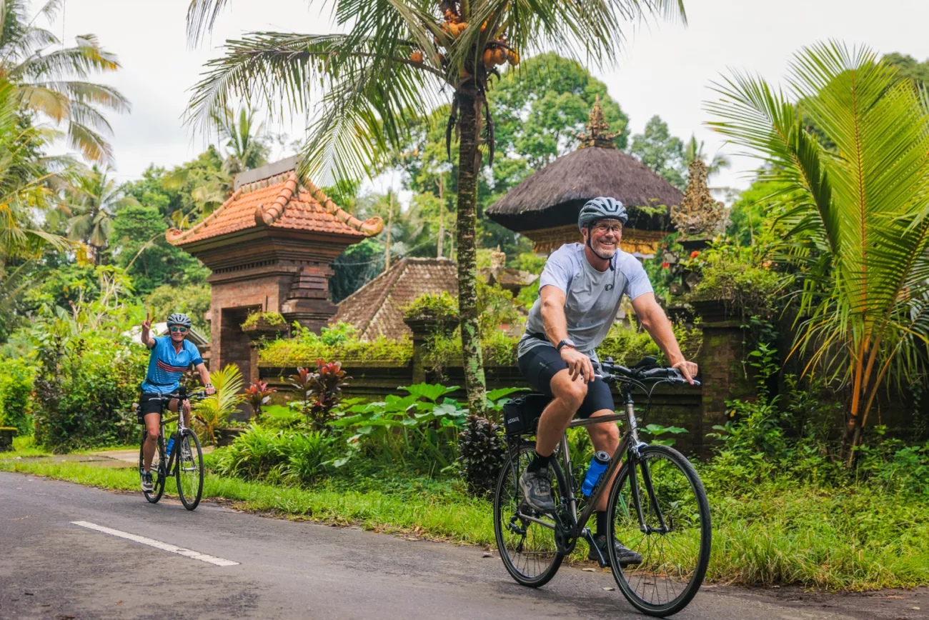 Man and woman biking on a road with jungle in the background
