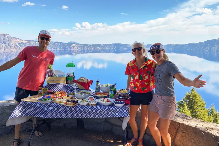 Three guests next to lunch table, large lake in background.