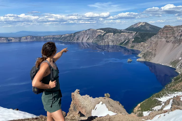 Guest on cliff's edge, pointing towards Crater Lake.