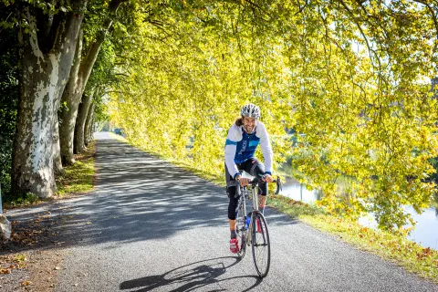 Guest/leader cycling down tree-covered road, smiling.