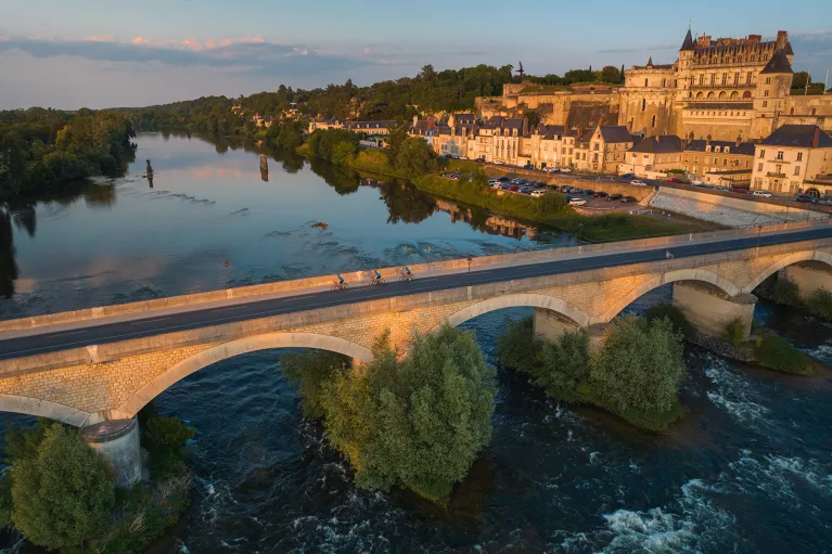 Bird's eye shot of cyclists over Loire River during sunset.  Château Royal d'Amboise behind.