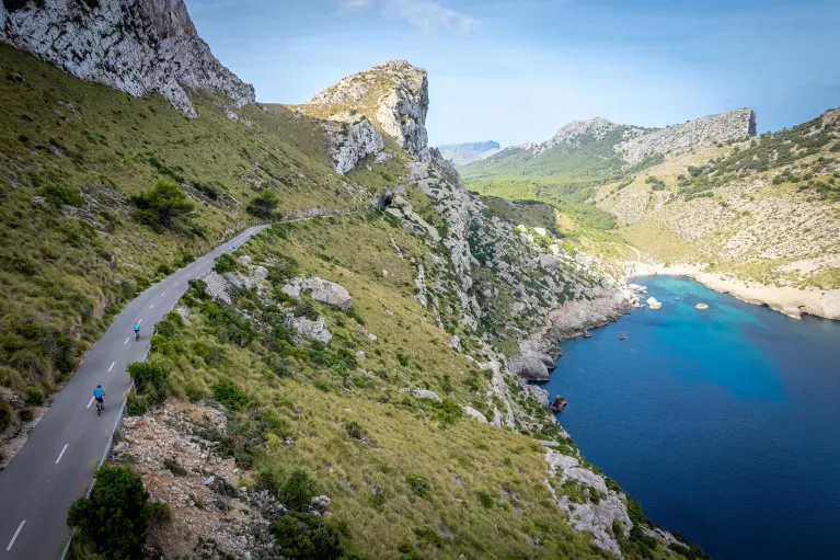 Two bikers riding around a bend on the coast of Mallorca.