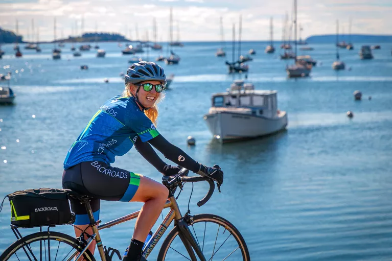 Guest biking with ocean and ships in background.