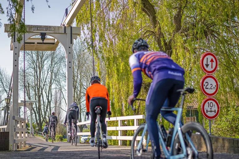 Five cyclists biking across a wooden bridge.