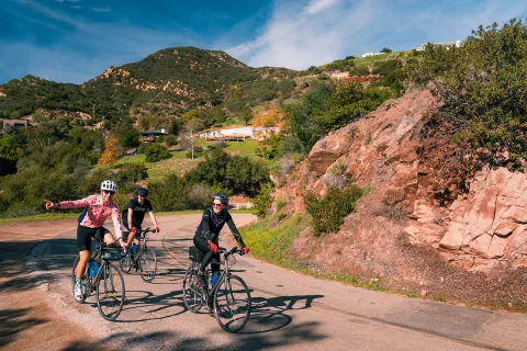 Three guests rounding corner, one pointing towards camera, Cali hills in background.