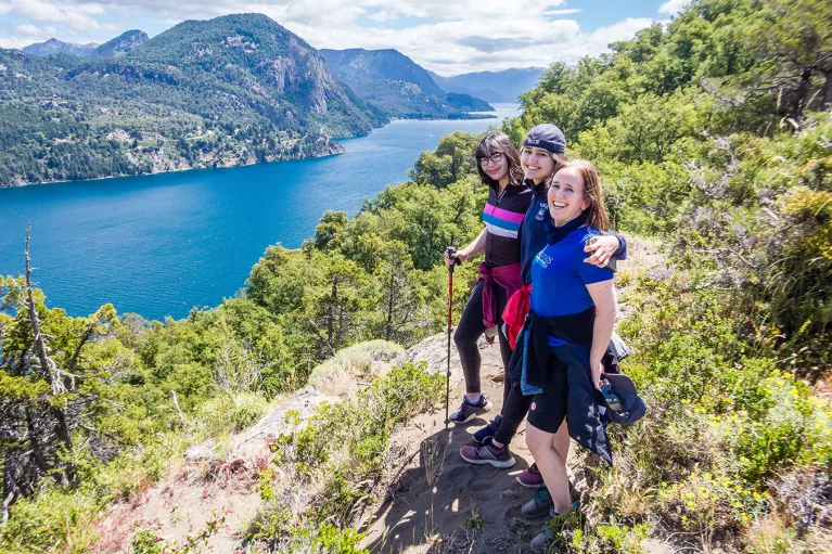Three young guests posing together, overlooking large lake, hillside.