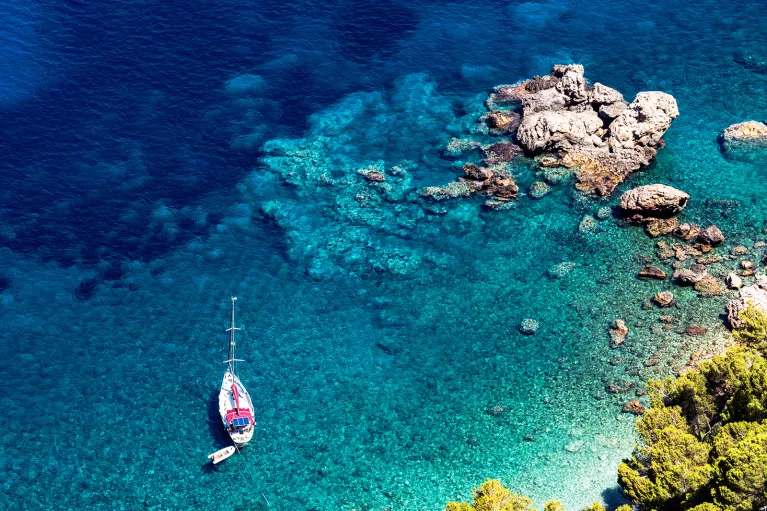 Bird's eye shot of rocky beach, small boat, blue water.