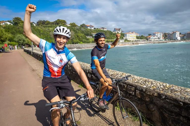 Two guests, cycling with fists raised, ocean to left.