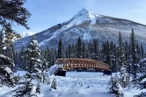 Wide shot of snowy bridge, Rockies in background.