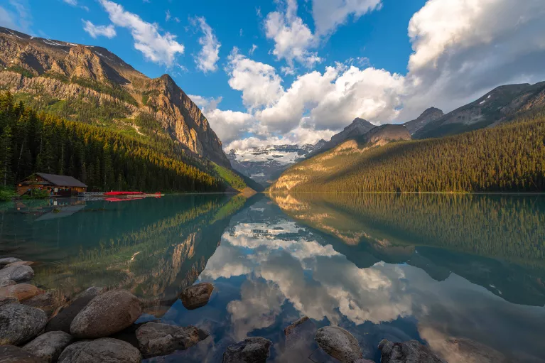 Wide shot of lake, wooden shack, mountain range, valley.