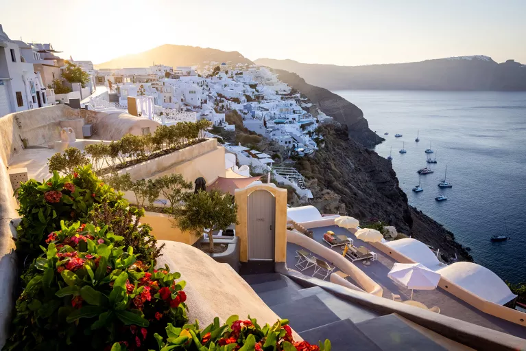 Wide shot of Santorini cliffside, white houses, ocean, sunset.