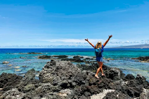 Woman walking towards the ocean with her arms in the air