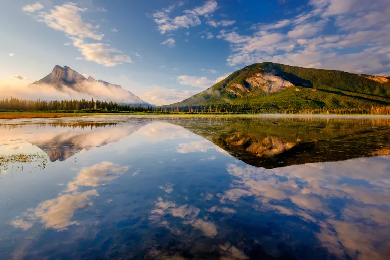 Wide shot of reflective lake, mountains during sunset.