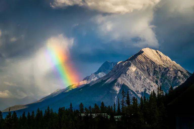 Shot of mountain range, clouds, rainbow visible.