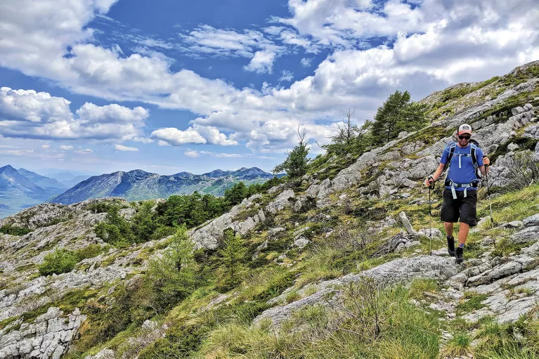 Guest hiking on craggy hillside, cloudy sky behind them.