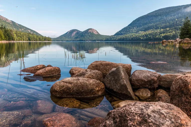 Wide shot of reflective lake, rounded mountains.