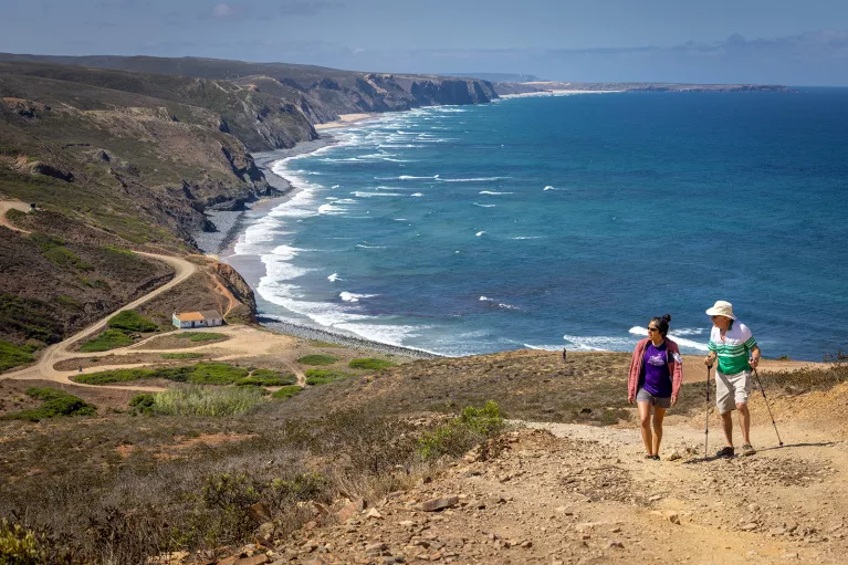 Two hikers walking up a sandy hill with the ocean in the background