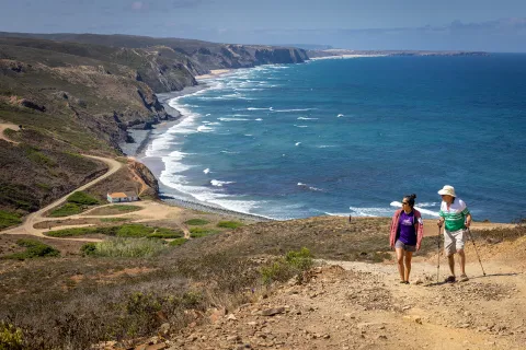 Two hikers walking up a sandy hill with the ocean in the background