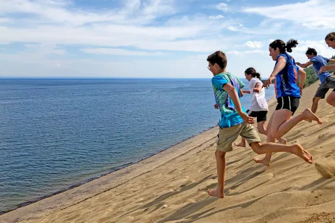 Group of young guests running down sand dune towards ocean.
