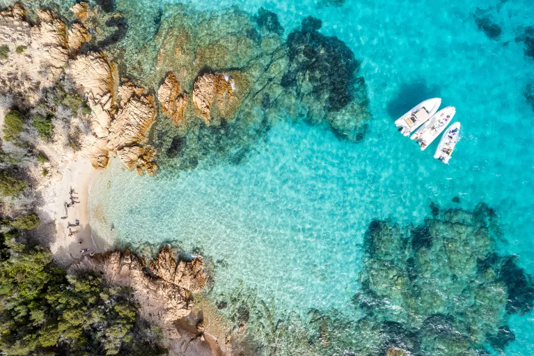 Overhead shot of guests on the beach, some are on small boats in the water.