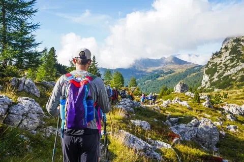 Group of guests hiking down mountain trail, cloudy mountainous vista in distance.