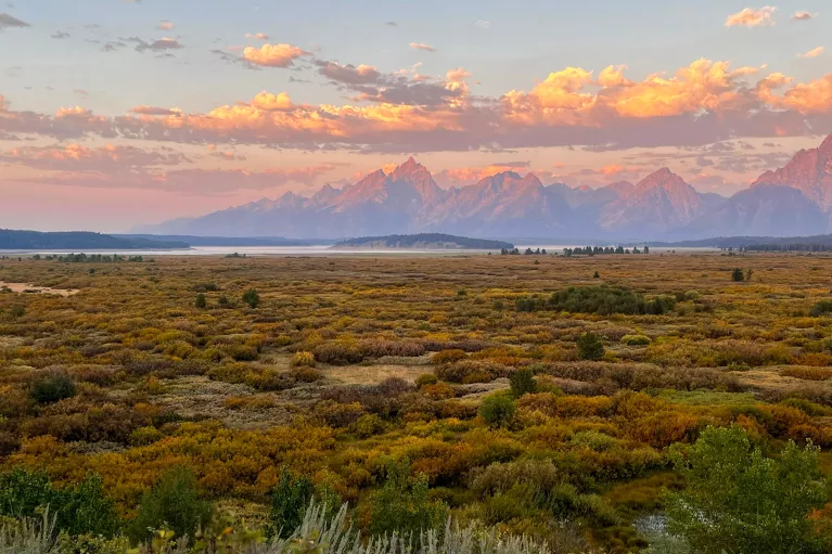 Purple and orange sunset with scenic green field and rocky mountains