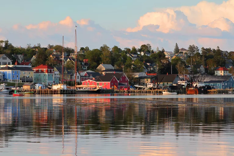 Wide shot of seaside town at sunset, vibrant red houses scattered throughout.