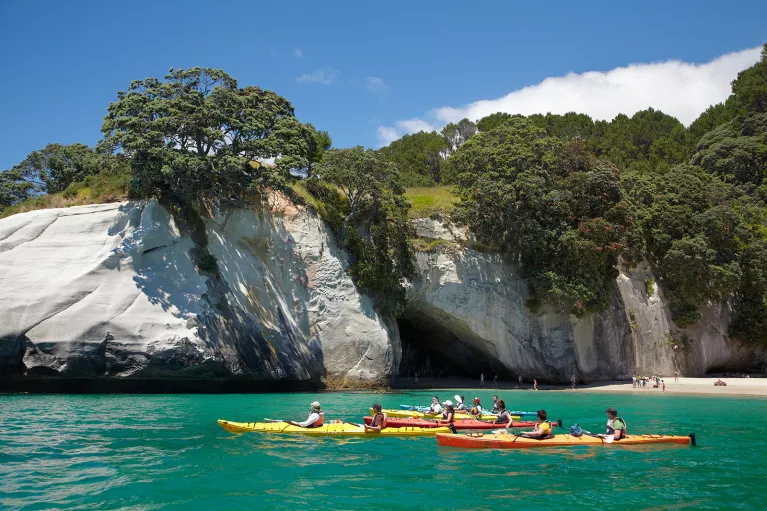 Guests kayaking away from beach, white stone cliff behind them. 