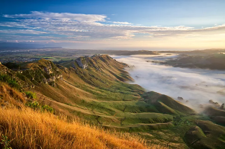 Wide shot of cloud covered valley during sunset, sloping cliffs rising from it.