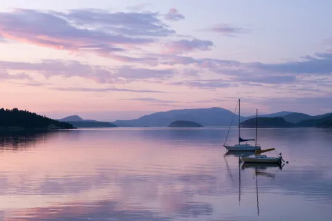 Two sailboats on a still lake during purple sunset.