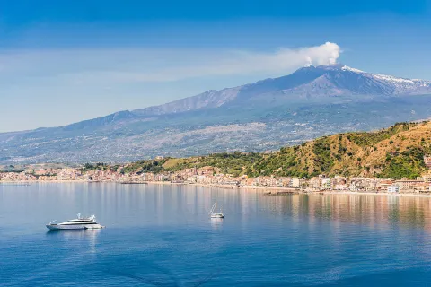 Wide shot of Mount Etna, small boats in water in foreground.