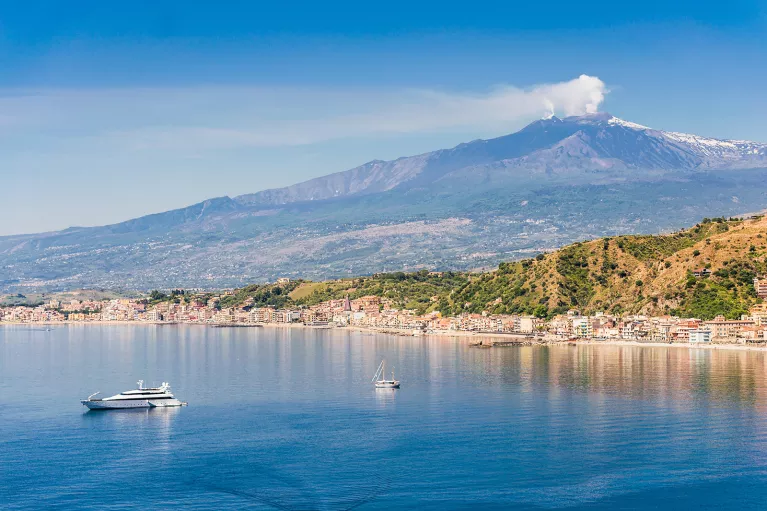 Wide shot of Mount Etna, small boats in water in foreground.