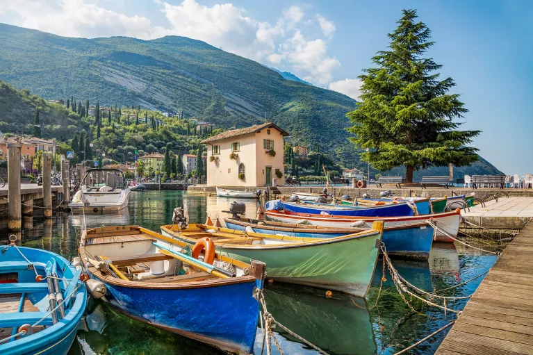 Small coastal pier, colorful ships visible, mountain in distance.