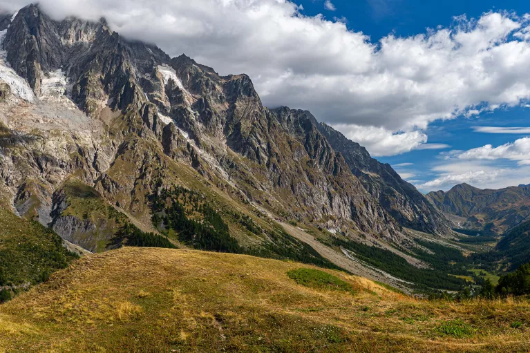 Wide shot of craggy mountains, golden hills in foreground. 