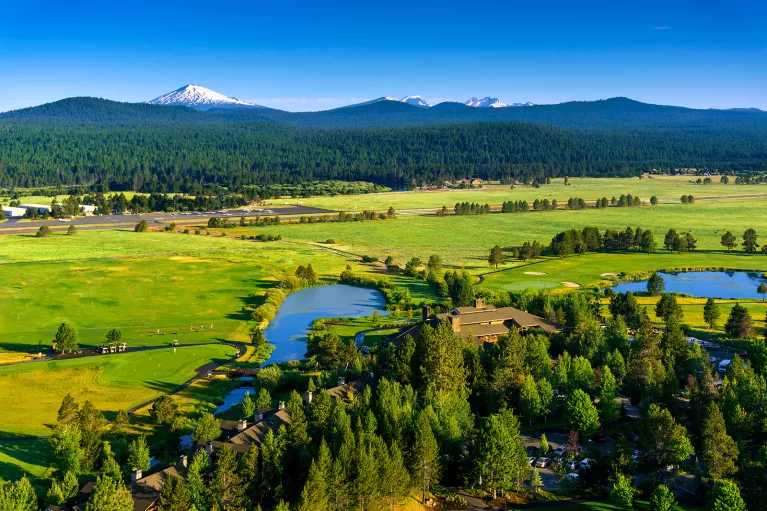 Wide shot of green pasture, large house in foreground, mountains in background.
