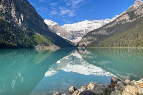 Wide shot of blue lake, mountains, clouds, sky.