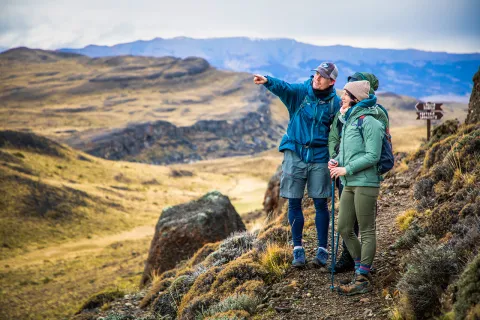 Three guests on hillside trail, one pointing towards something off-frame. 