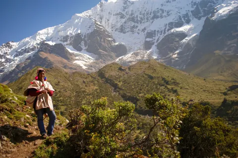 Local on hillside playing instrument, snowy mountains, hills behind them.