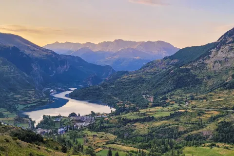 Wide shot of mountain valley town, river running through, sunset.